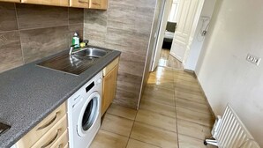 Une cuisine compacte avec des meubles en bois, un lave-linge encastré et un plan de travail gris.