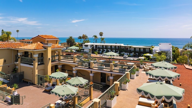 A resort with multiple-story buildings, outdoor seating areas with umbrellas, and a view of the ocean. - Boutique Hotel | Rooftop Ocean Views + Pool + Hot Tub | Walk to Everything (Laguna Beach)