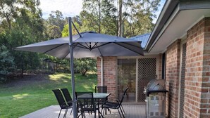 Un patio con tavolo e sedie, un barbecue e una zona coperta con un ombrello.