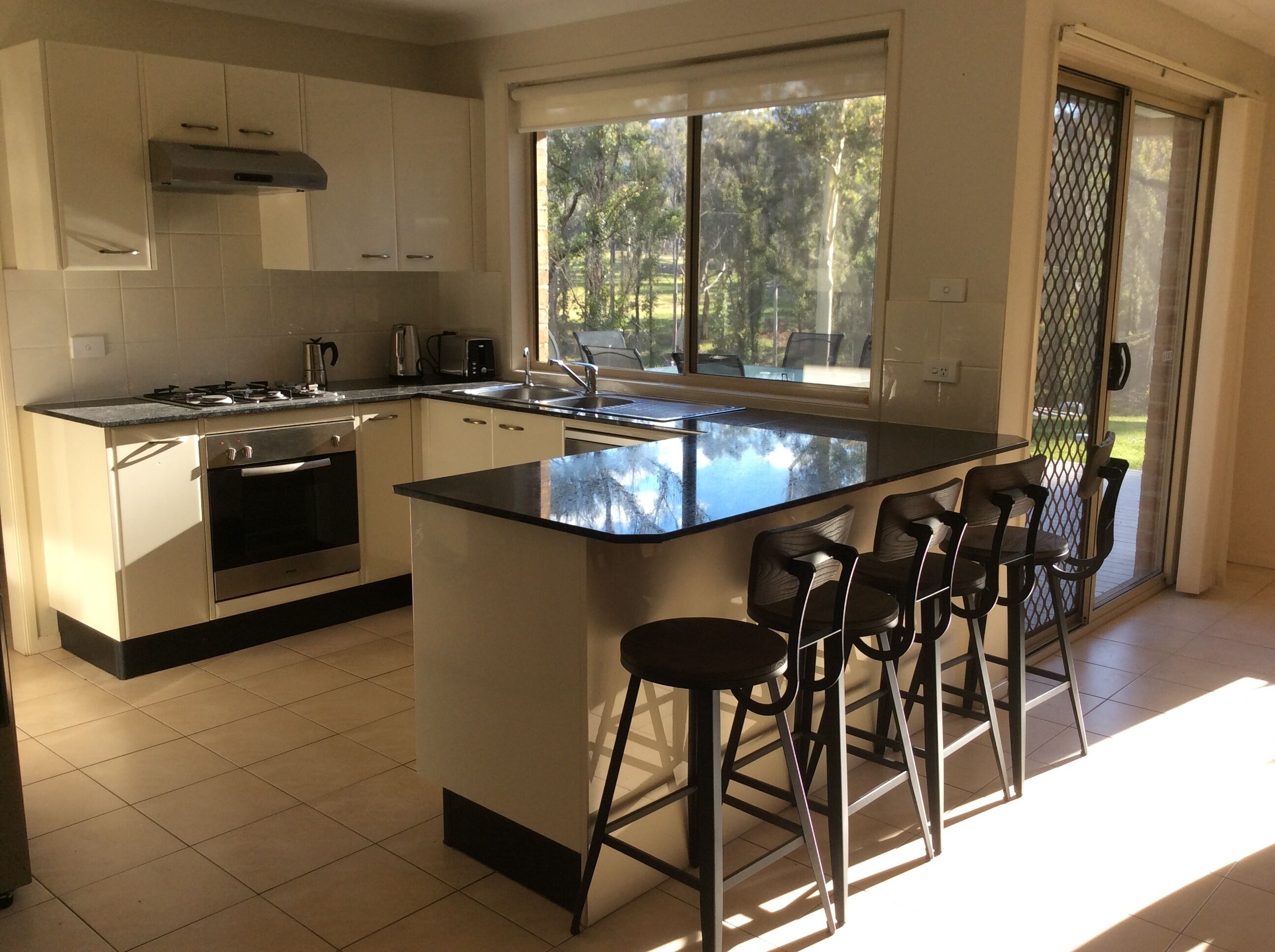 A modern kitchen with a large island, bar stools, and a view of the outdoors through a sliding door.