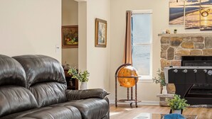 A living room with a leather sofa, a globe on a stand, a fireplace, and a window with a view. - Mount Pocono Escape • Firepit + Game Room • Near Trails + Lakes | Poconos Fun (Mount Pocono)