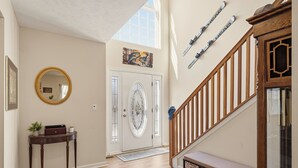 A hallway with a wooden floor, a white door with a glass panel, a mirror, and a staircase with wooden railings. - Mount Pocono Escape • Firepit + Game Room • Near Trails + Lakes | Poconos Fun (Mount Pocono)