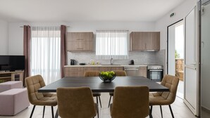 A modern kitchen with a dining area, featuring a large table, chairs, and a fruit bowl. - Elysian Luxury Residence -Melia (Stegna)