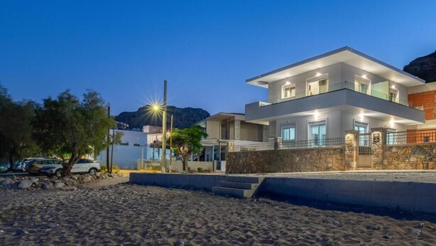 A modern two-story house with a balcony, a stone wall, and a car parked nearby. - Elysian Luxury Residence -Melia (Stegna)