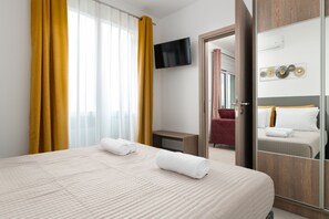 A hotel room with a bed, a TV mounted on the wall, a mirror, and a door leading to another room.