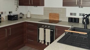 A modern kitchen with wooden cabinets, a stainless steel range hood, a built-in oven, and a countertop with a coffee maker and toaster. - Central Belfast Apartment/Modern/Ideal for Work & Leisure (Belfast)