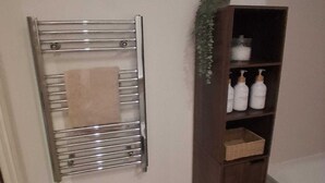 A bathroom with a towel rack, a wooden shelf with toiletries, and a green rug. - Central Belfast Apartment/Modern/Ideal for Work & Leisure (Belfast)