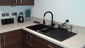 A kitchen with dark wooden cabinets, a black sink, and a coffee-themed wall decoration. - Central Belfast Apartment/Modern/Ideal for Work & Leisure (Belfast)