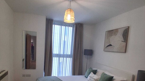 A bedroom with a bed, bedside tables, a lamp, a window with curtains, a wall-mounted artwork, and a ceiling fan. - Central Belfast Apartment/Modern/Ideal for Work & Leisure (Belfast)