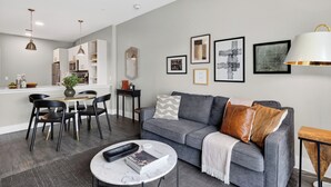 Ein modernes Wohnzimmer mit einem grauen Sofa, schwarzen Sesseln, einem Couchtisch und einem Essbereich mit einem weißen Tisch und Stühlen.