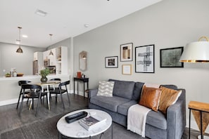Ein modernes Wohnzimmer mit einem grauen Sofa, schwarzen Sesseln, einem Couchtisch und einem Essbereich mit einem weißen Tisch und Stühlen.