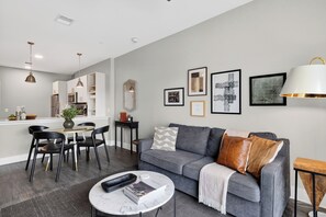 Ein modernes Wohnzimmer mit einem grauen Sofa, schwarzen Sesseln, einem Couchtisch und einem Essbereich mit einem weißen Tisch und Stühlen.