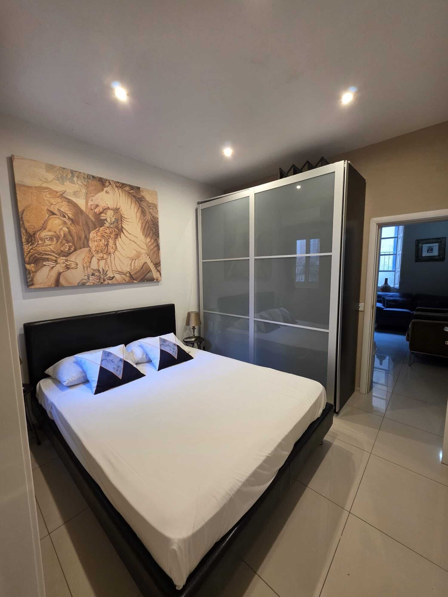 Un dormitorio moderno con una cama grande, un armario con puerta corredera de vidrio y un cuadro grande en la pared.