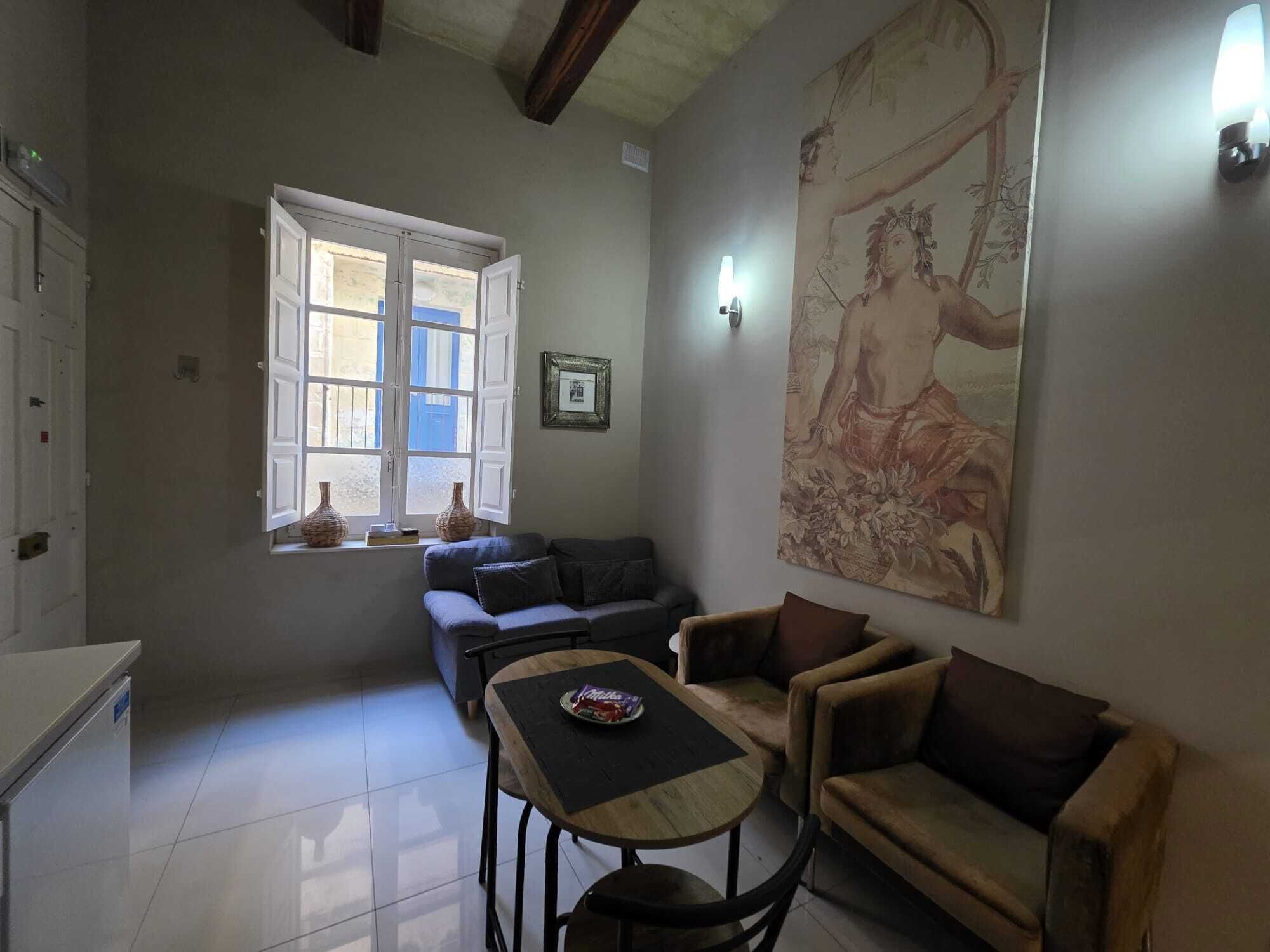 Una sala de estar con un sofá, una mesita, una ventana con persianas abiertas y un cuadro grande en la pared.