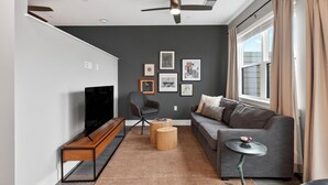 Un salon moderne avec un canapé, un téléviseur, un ventilateur de plafond et des tableaux encadrés accrochés au mur.