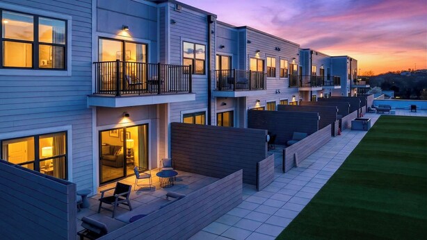 Un immeuble résidentiel moderne à plusieurs étages, doté de balcons, d’un espace extérieur aménagé pour s’asseoir et d’une pelouse bien entretenue.