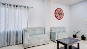 A living room with a sofa, a glass coffee table, a patterned curtain, and a decorative wall piece. - Super Townhouse Isbt Guwahati (Guwahati)