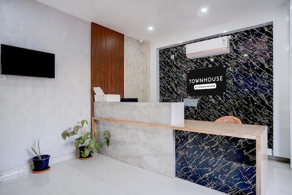 A reception desk with a sign reading 'Townhouse Company-Serviced,' a flat-screen TV mounted on the wall, and a potted plant on the floor.