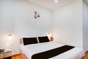 A neatly made bed with white bedding and a black accent, a bedside table with a lamp, and a wall-mounted light fixture.