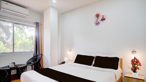 A bedroom with a bed, bedside table, lamp, and a window with curtains. - Super Townhouse Isbt Guwahati (Guwahati)