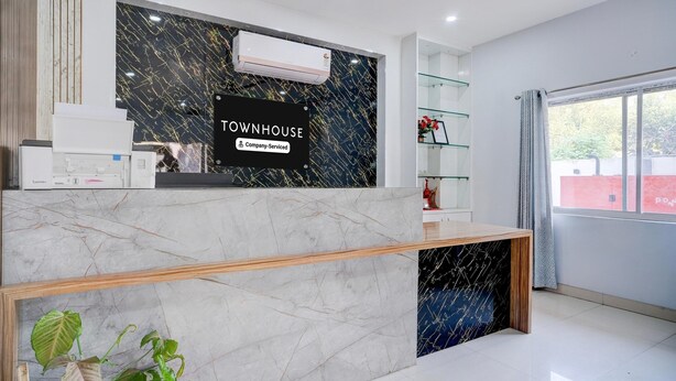 A reception desk with a sign reading 'TOWNHOUSE,' a mounted air conditioner, and a plant in the foreground. - Super Townhouse Isbt Guwahati (Guwahati)