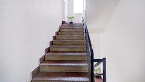 A staircase with a handrail, a potted plant on the landing, and a window at the top. - Super Townhouse Isbt Guwahati (Guwahati)