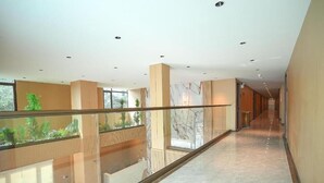 A modern hotel interior with a glass railing, a marble floor, and a view of greenery outside. - VELIN Pattaya Hotel-Family 2 (Nong Prue Subdistrict)