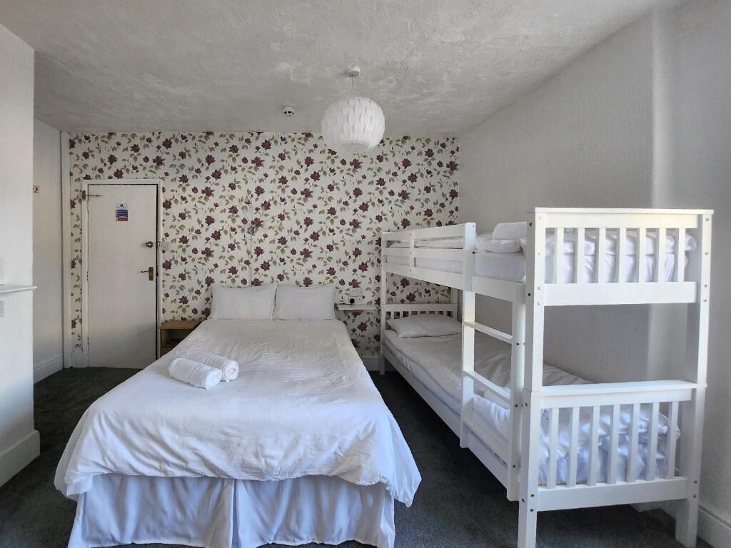 A room with a bunk bed, a single bed, floral wallpaper, a white door, and a white ceiling light.