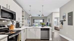 Una cucina moderna con microonde, fornelli e lavastoviglie, un'area pranzo con una pianta, e vista sulla città.