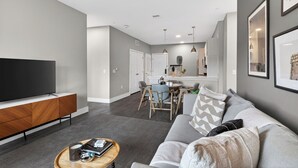 A modern living room with a flat-screen TV, a wooden entertainment unit, a grey sofa, and a coffee table. - Walkable + Terrace | Hillsboro Village, Nashville | Belcourt (Nashville)