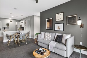 Ein modernes Wohnzimmer mit einem grauen Sofa, einem Couchtisch und einem Essbereich mit Stühlen und Tisch.