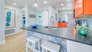 Una cucina moderna con isola centrale, sgabelli da bar bianchi e una ciotola decorativa blu.