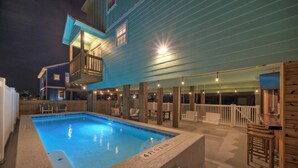 Una piscina con bordo in legno e zona relax coperta.