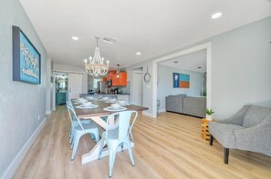 Amplia sala de estar con una mesa de comedor dispuesta para seis personas, un sofá gris y un sillón estampado.