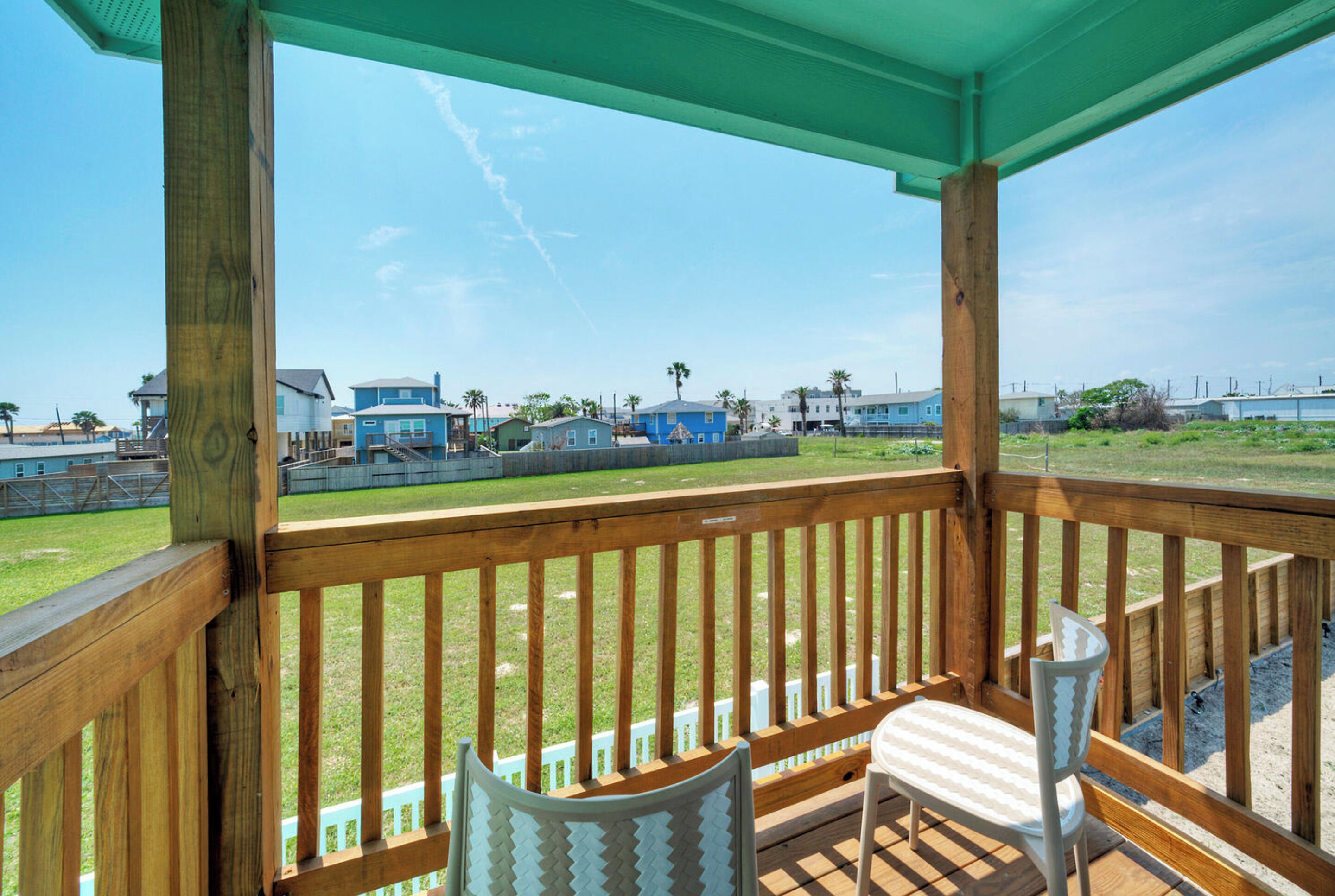 Una terraza de madera con dos sillas, con vistas a un área verde con casas y un cielo despejado.