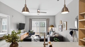 A modern kitchen with a central island, pendant lights, a ceiling fan, and a view to a living area with a sofa and coffee table. - ADA Unit | Rooftop Lounge | Walk to Vanderbilt + Music Row | Hillsboro Village (Nashville)