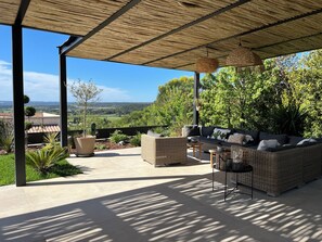 Une terrasse extérieure dotée d’un espace salon couvert, offrant une vue sur la campagne et agrémentée d’une pergola.