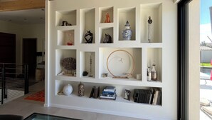 A modern interior with a glass-bottomed table, wooden beams, and a white wall with shelves displaying various items. - Contemporary Villa with Unobstructed View & Pool (Éguilles)