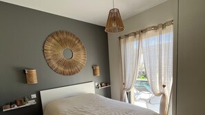 A bedroom with a large bed, a wall-mounted circular mirror, a hanging light fixture, and a window with sheer curtains. - Contemporary Villa with Unobstructed View & Pool (Éguilles)
