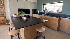A modern kitchen with a central island, bar stools, pendant lighting, and a view through a window. - Contemporary Villa with Unobstructed View & Pool (Éguilles)