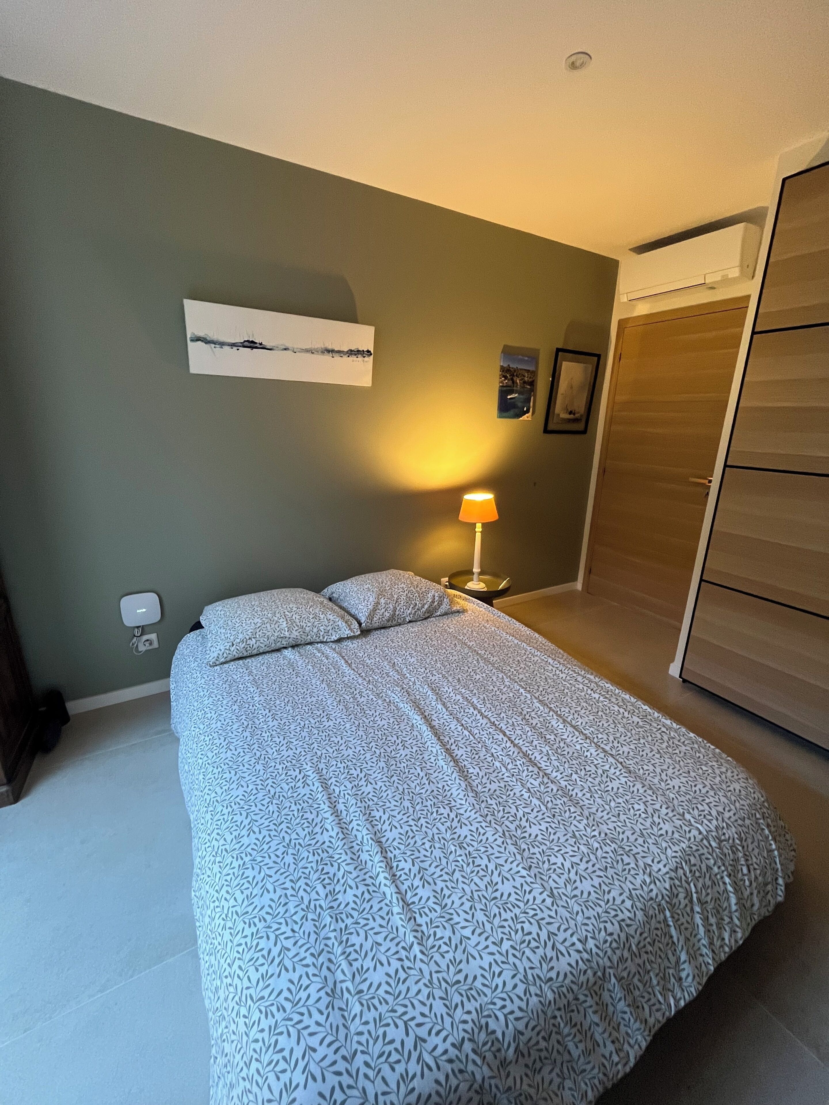 A bedroom with a bed, a bedside lamp, a wall-mounted artwork, and a wardrobe.