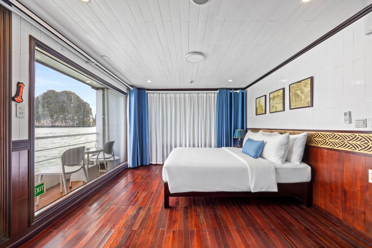 Una habitación con una cama, vistas al agua, una ventana con cortinas y una puerta con letrero de salida.