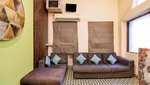 A room with a brown sofa set, a television, an air conditioning unit, and a patterned floor. - Classic Hotel Venkateshwara (Kolkata)