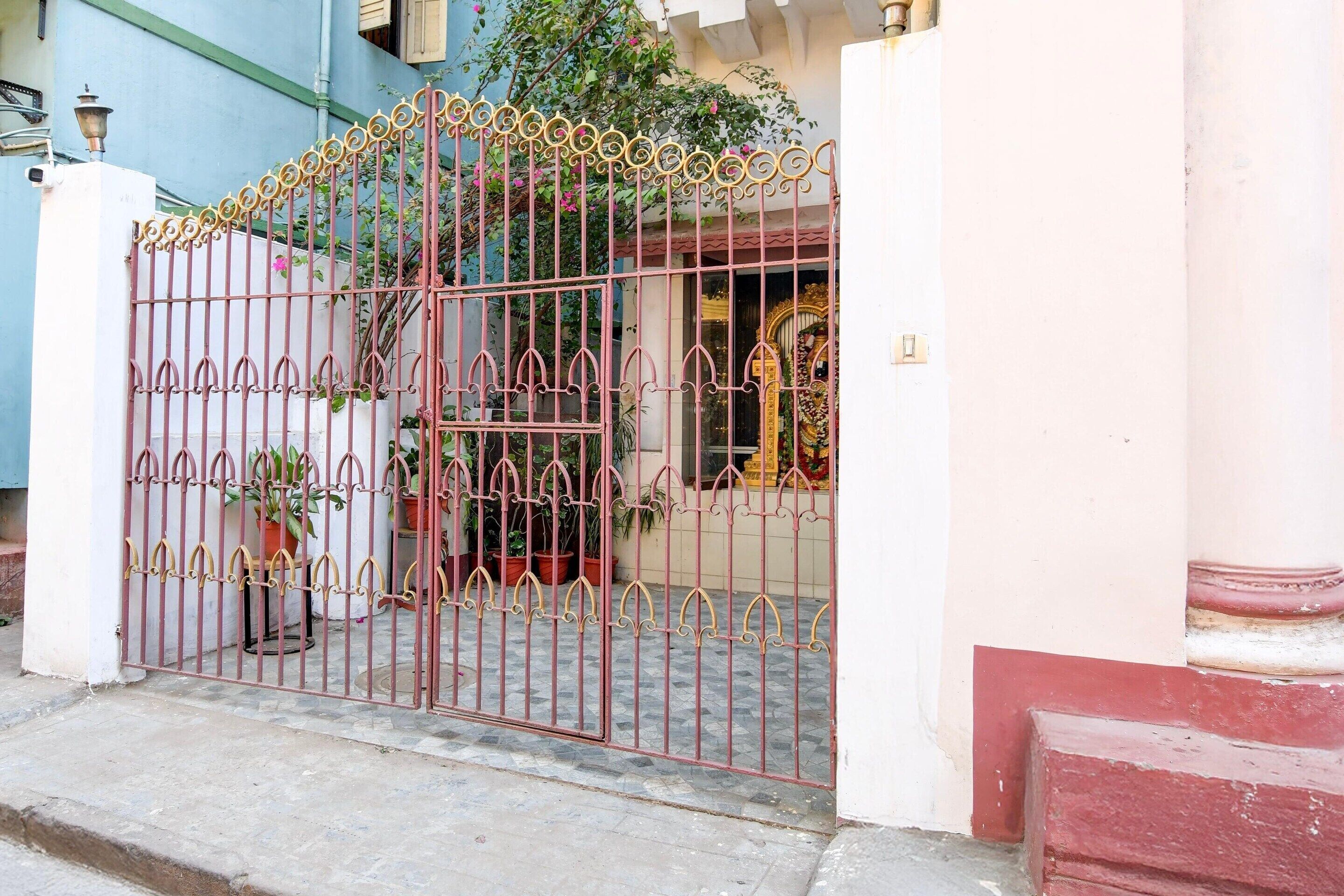 A gated entrance with a decorative iron gate, potted plants, and a building facade.