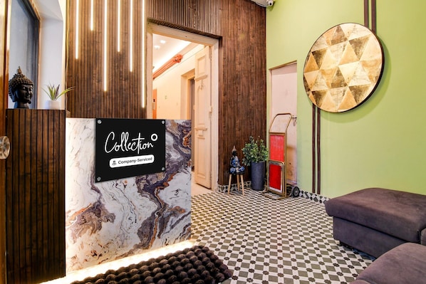Un espace d’accueil avec un mur en marbre, une enseigne indiquant « Collection », un sol à carreaux et un élément décoratif circulaire sur le mur.