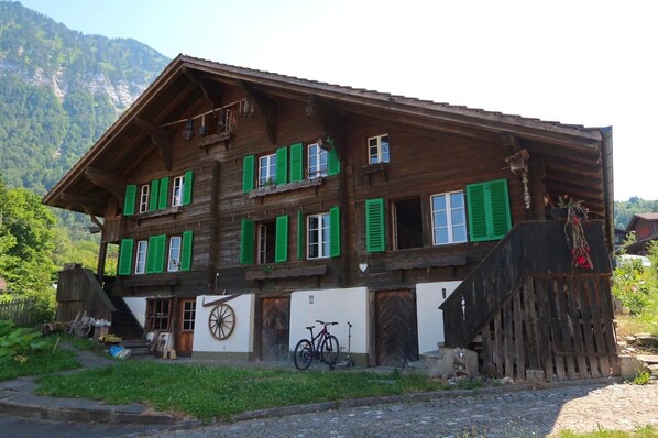 A wooden chalet with green shutters, a bicycle, and a mountain backdrop. - Lakeview Chalet 1 , Därligen (Interlaken-Oberhasli)