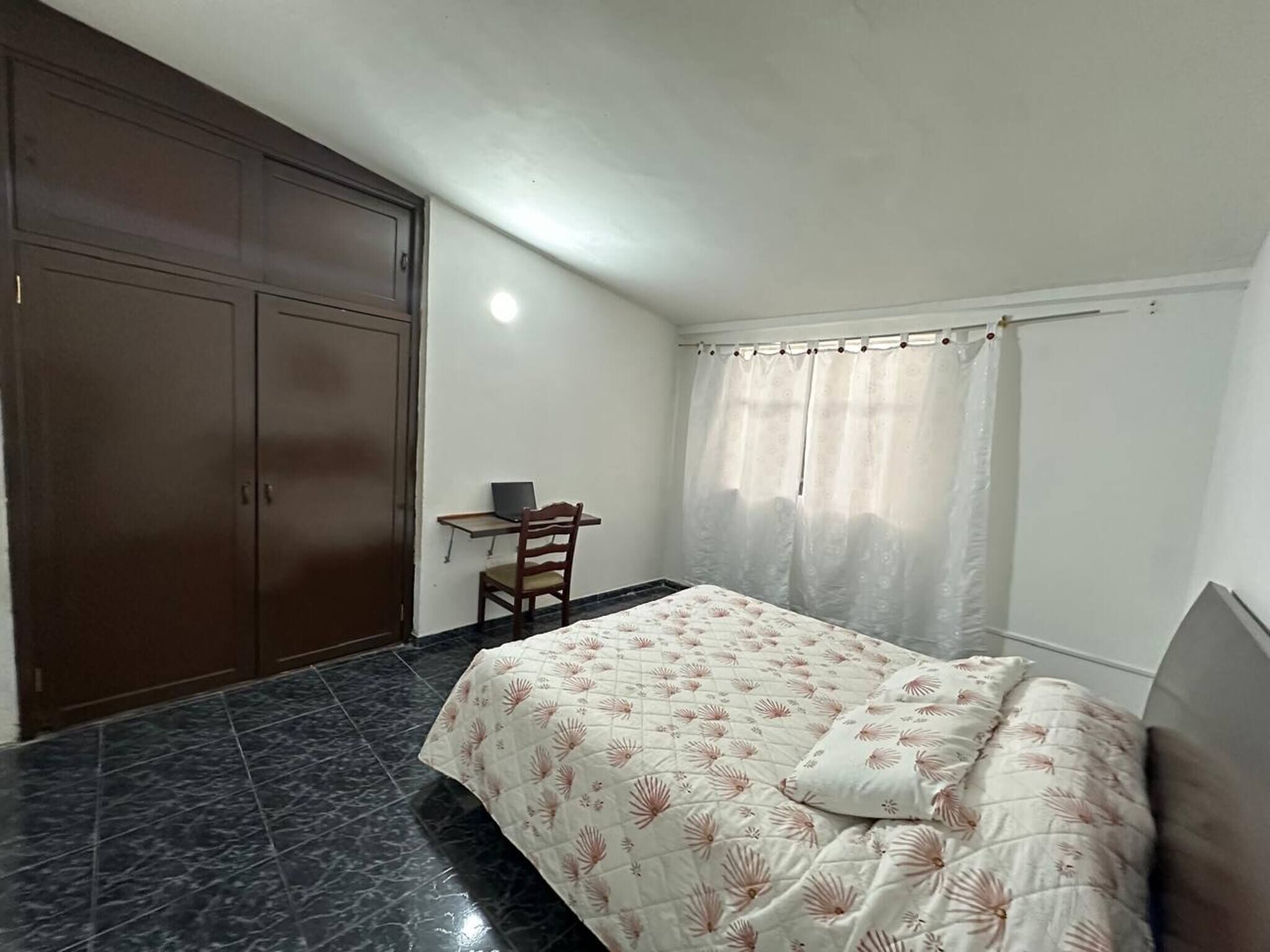A bedroom with a bed, a desk, and a wardrobe.