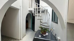 A narrow hallway with a white archway, a staircase, and a potted plant on a black surface.