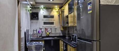 A modern kitchen with stainless steel appliances, a black countertop, and a tiled floor.