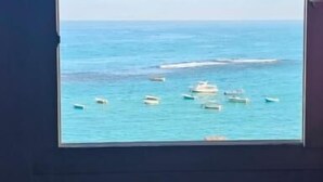 A room with a large window overlooking a calm sea, a dark-colored sofa, and a dark wall. - شقة فندقية لعشاق الذوق الرفيع Luxury Flat In Miami with panoramic sea views (Alexandria Governorate)